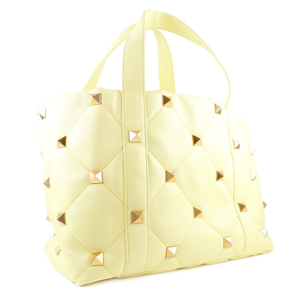 Light yellow quilted handbag with stud details on a white background